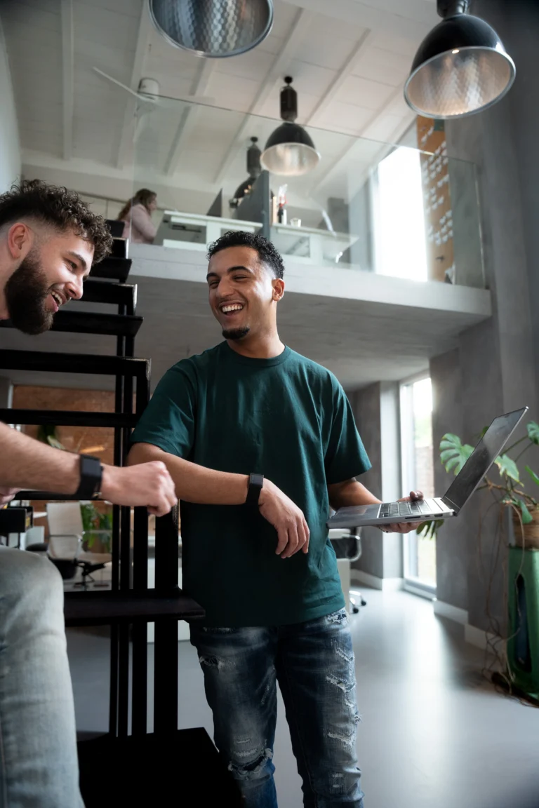 Twee collega's lachen samen bij de trap op kantoor
