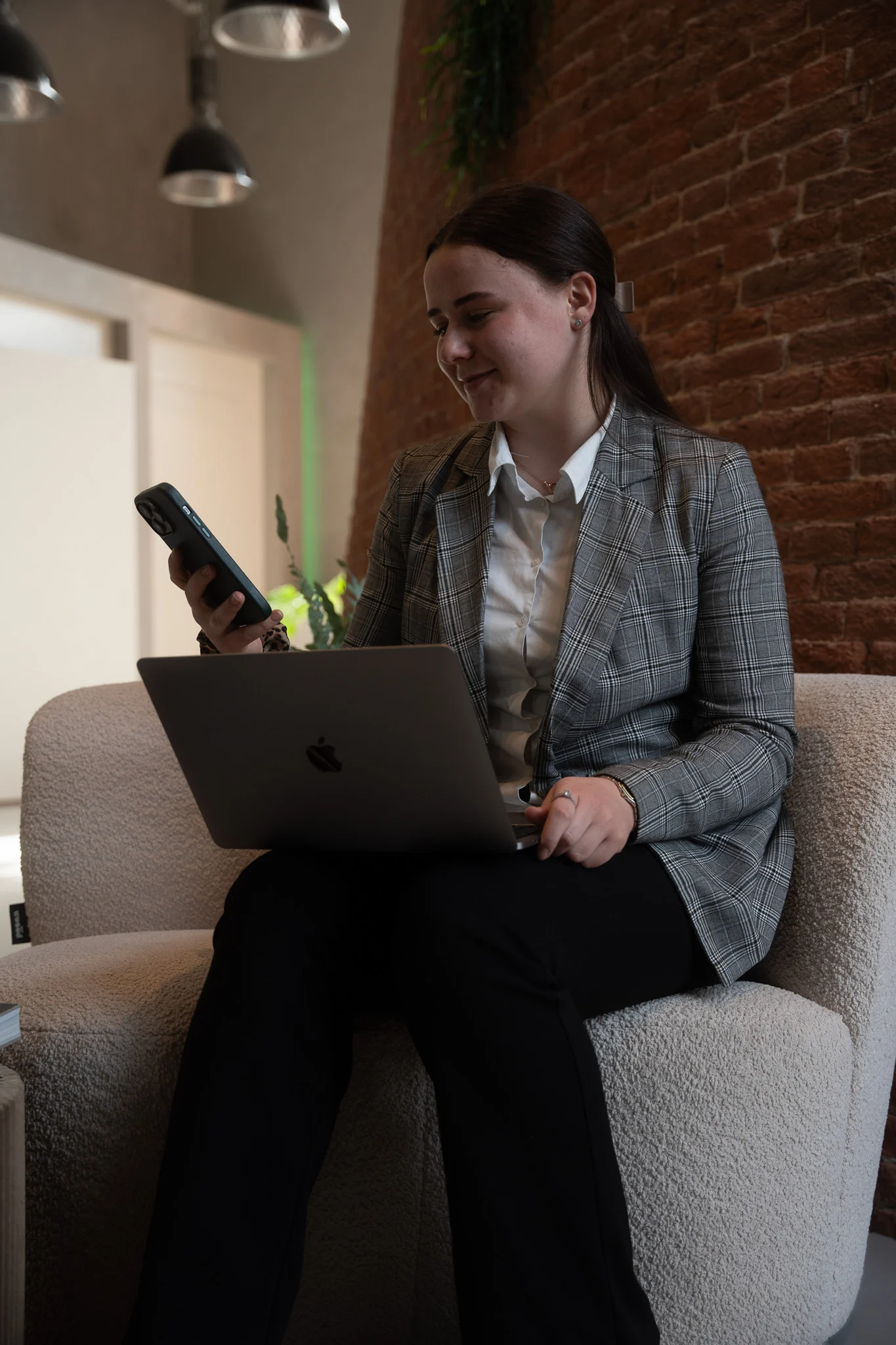 Collega werkt met laptop en telefoon vanuit een fauteuil