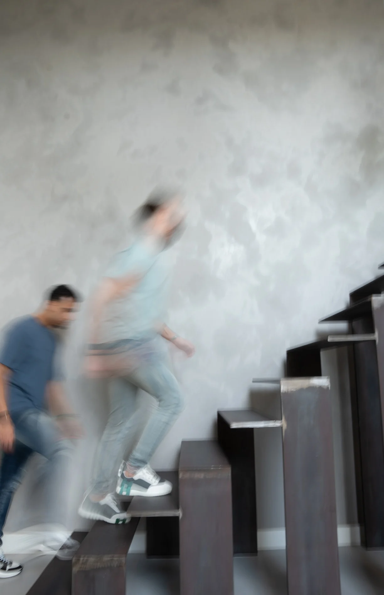 Twee mensen lopen in vaart een zwevende houten trap op langs een betonnen wand