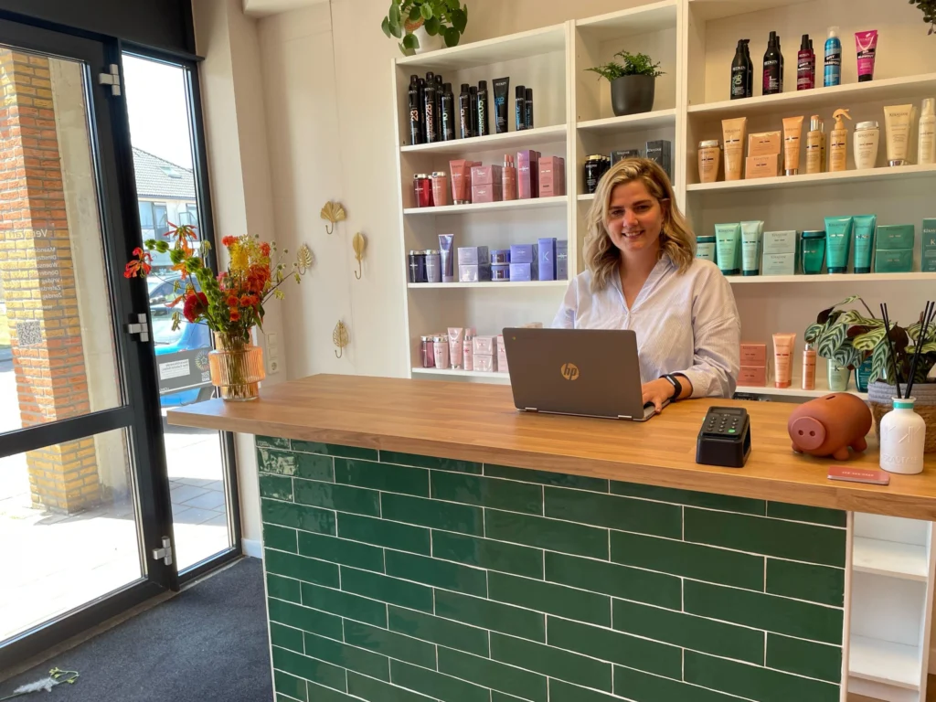 Ondernemer met laptop achter de toonbank van haar winkel